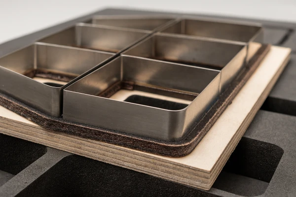 Close-up view of a steel rule die cutting EVA foam inserts for electronic packaging, showing precise cavities and clean edges on the flatbed die cutter.